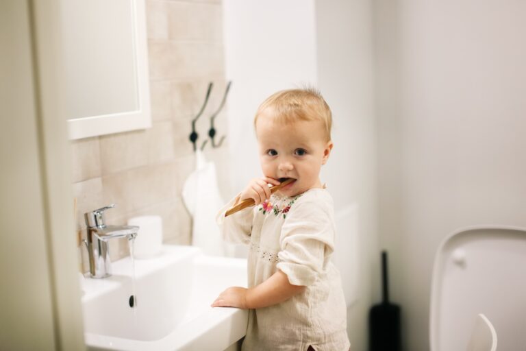Cute caucasian Toddler kid Cleans Teeth by Bamboo Toothbrush by Bathroom Sink